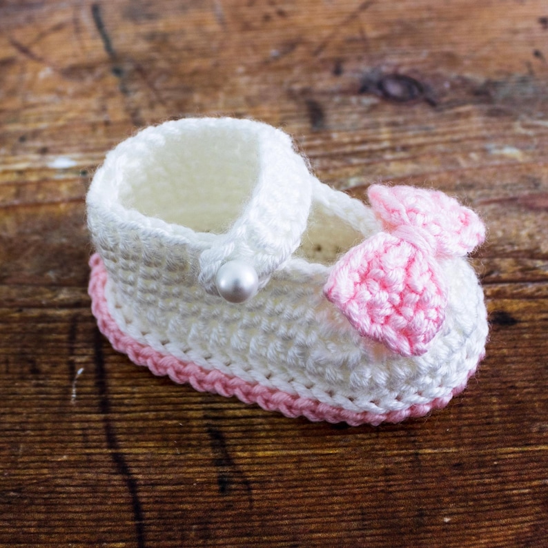 May include: White crocheted baby shoe with a pink bow and a pearl accent.