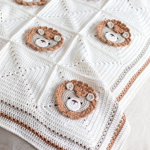 May include: A white crocheted baby blanket with a brown crocheted lion face design. The blanket has a brown crocheted border.