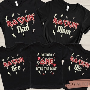 May include: Black t-shirts with a rock and roll theme. The shirts feature the words "Rockin' Dad", "Rockin' Mom", "Rockin' Bro", "Rockin' Sis", and "Another One Bites the Dust".
