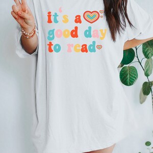 K&ouml;nnte beinhalten: Wei&szlig;es Oversize-T-Shirt mit dem Text "it's a good day to read" in bunter Retro-Schriftart mit einem Herz-Motiv.