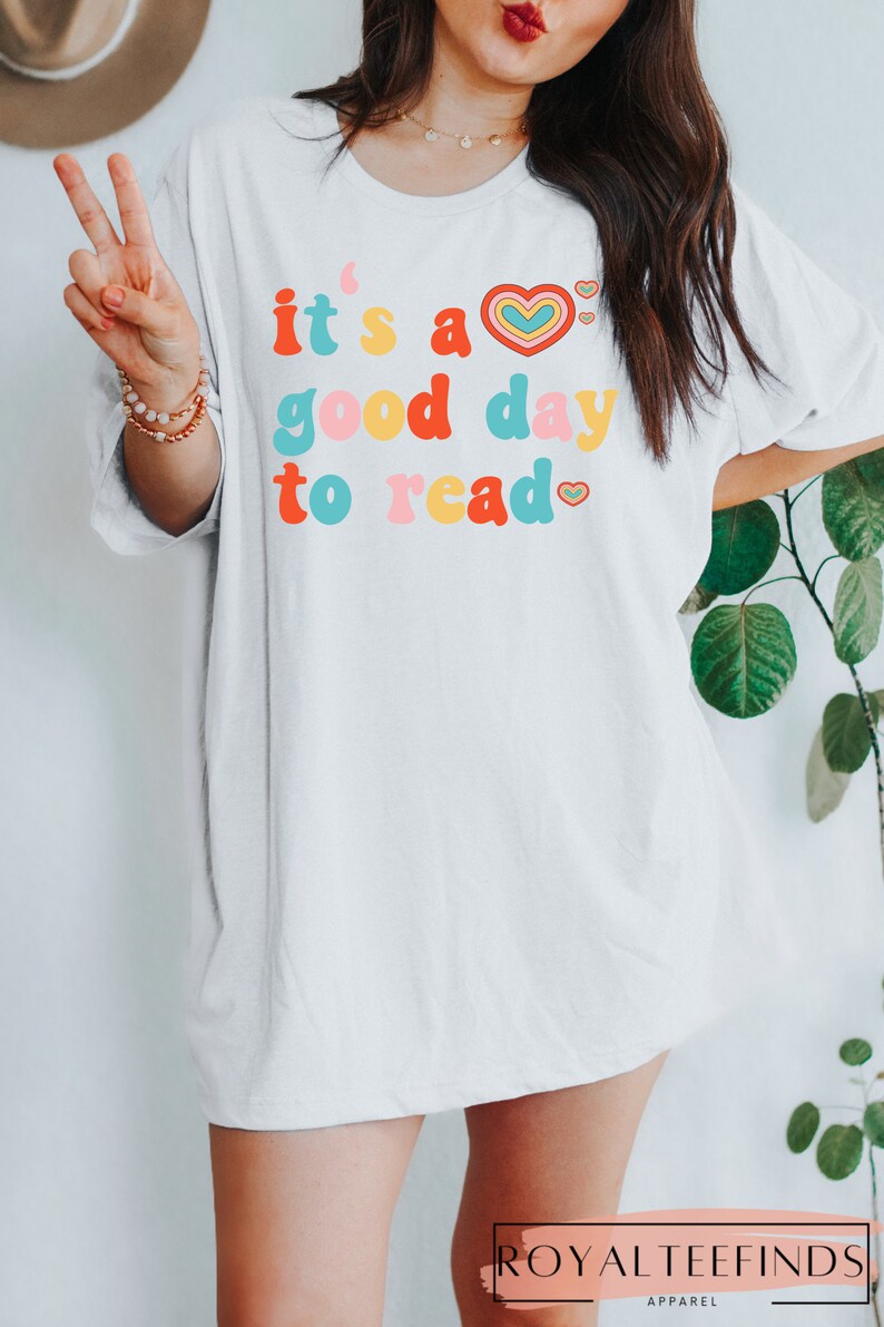 K&ouml;nnte beinhalten: Wei&szlig;es Oversize-T-Shirt mit dem Text "it's a good day to read" in bunter Retro-Schriftart mit einem Herz-Motiv.