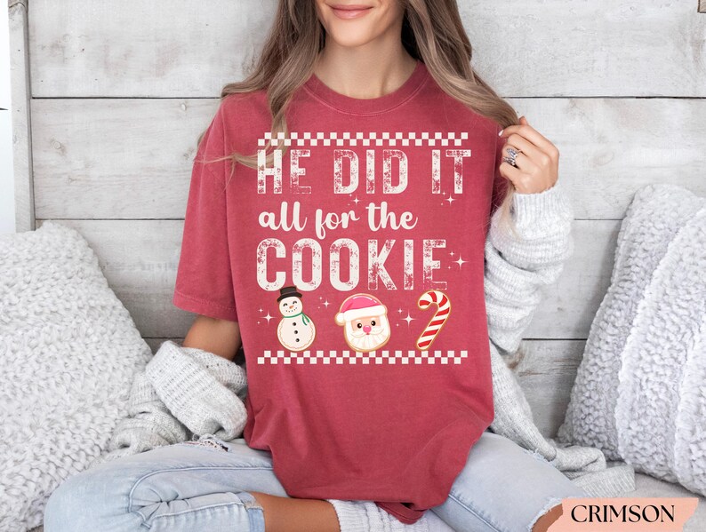 Op de afbeelding: Karmizijnrood T-shirt met de tekst "HE DID IT all for the COOKIE". Het shirt heeft koekjesontwerpen van een sneeuwpop, de kerstman en een zuurstok. Het shirt heeft een relaxte pasvorm.