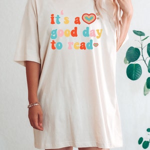 K&ouml;nnte beinhalten: Ein wei&szlig;es Oversize-T-Shirt mit dem Text "it's a good day to read" in bunten Buchstaben mit Herzen.