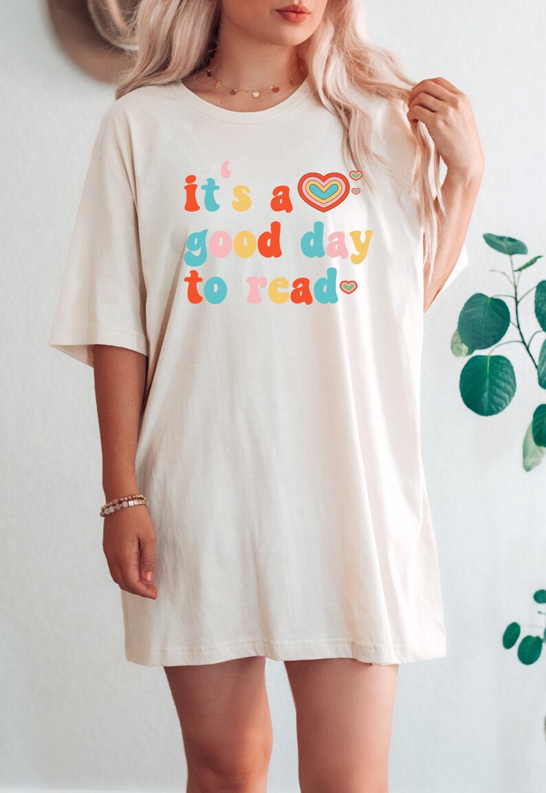 K&ouml;nnte beinhalten: Ein wei&szlig;es Oversize-T-Shirt mit dem Text "it's a good day to read" in bunten Buchstaben mit Herzen.