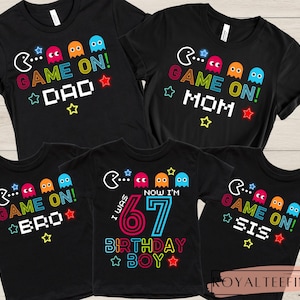 May include: Black t-shirts with colorful "Game On!" designs. The shirts feature Pac-Man-style graphics and text for Dad, Mom, Bro, Sis, and a birthday boy. The designs include stars and colorful ghosts.