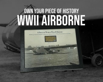 May include: A black framed photo of a WWII era glider plane with the text "A Piece of World War II History" and "WWII Operation Market Garden Airborne Division Waco CG-4A Glider Canvas Fabric" printed below the image.
