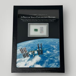 May include: A framed display featuring a fragment of an International Space Station computer board. The display includes a photo of the ISS orbiting Earth, with text reading "A Piece of Space Exploration History."