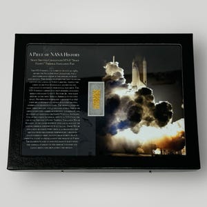 May include: A piece of NASA history, a small piece of thermal insulation from the Space Shuttle Challenger STS-7, flown on August 29, 1983. The image shows the shuttle launching with a trail of smoke and fire.