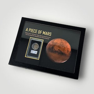May include: A black display case containing a piece of Mars. The case features a small, round specimen and a detailed depiction of the planet Mars. Text on the case reads "A Piece of Mars" and details about the specimen.