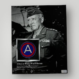 May include: A black and white photograph of General George S. Patton, Jr. in military uniform. He is wearing a cap with a patch that reads "A". The patch is a red circle with a blue centre and a white "A" in the centre. The text "A PIECE OF WORLD WAR II HISTORY" is below the image. The text "Original World War II 101st General Patton's Third Army Soldier's Uniform Patch" is below the text "A PIECE OF WORLD WAR II HISTORY".