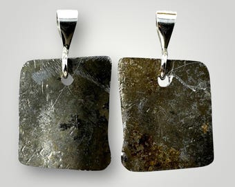 May include: Two silver pendants with square-shaped, dark gray, metallic pieces attached. The pieces have a rough, textured surface and appear to be made of metal.