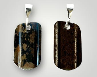 May include: Two silver pendant charms with a rustic, dark brown metal finish. The charms are shaped like dog tags and have a slightly rounded rectangular shape.