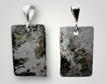 May include: Two silver pendants with a rectangular shape and a textured surface. The pendants have a silver bail and a hole at the top. The surface of the pendants is a mix of silver, black, and brown.
