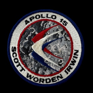 Puede incluir: Parche bordado con el logotipo de la misión Apolo 15. El parche tiene un diseño circular con las palabras "APOLLO 15", "SCOTT WORDEN IRWIN" y una imagen estilizada de una nave espacial en rojo, blanco y azul.