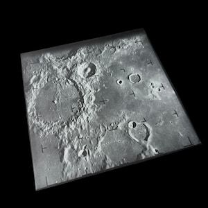 May include: A monochrome aerial photograph depicting the surface of the Moon, showing a multitude of craters. The image includes grid lines and crosshairs, possibly for mapping. The surface appears textured and detailed, with varying sizes of impact craters.