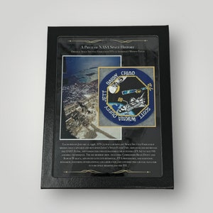 May include: A framed patch commemorating the STS-72 mission of the Space Shuttle Endeavour. The patch features a blue background with a white space shuttle and a yellow Earth. The text "Scott Jett Wakata Barry Chiao" is printed in white on the patch. The frame is black with a gold border. The text "A Piece of NASA Space History" is printed on the frame.