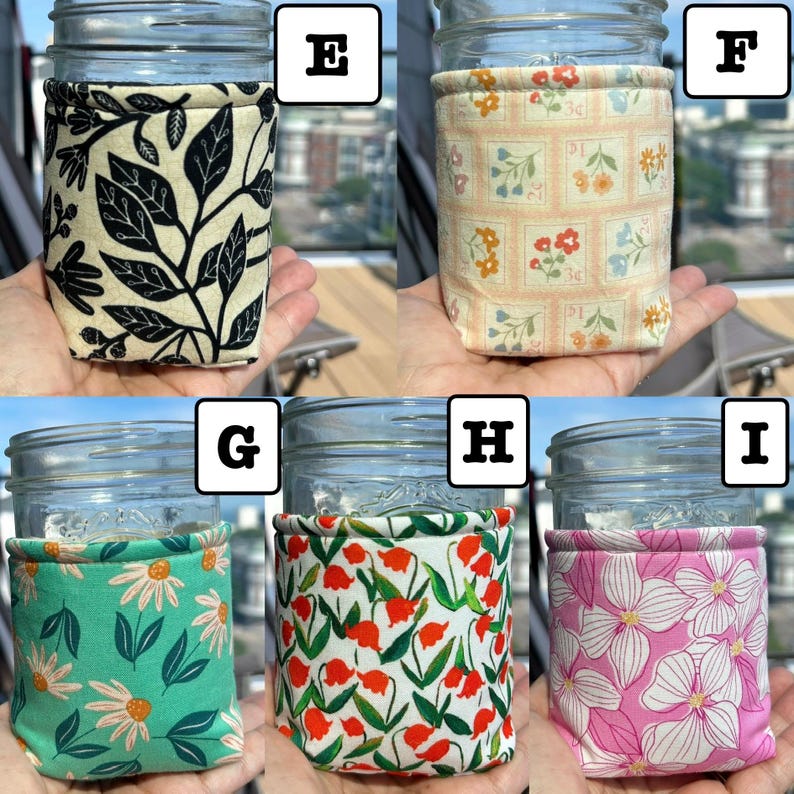 K&ouml;nnte beinhalten: F&uuml;nf Einmachgl&auml;ser aus Glas, jedes mit einer anderen Stoffh&uuml;lle umwickelt. H&uuml;lle E zeigt schwarze Bl&auml;tter auf cremefarbenem Grund. F hat ein Gitter aus Blumenbriefmarken. G zeigt wei&szlig;e G&auml;nsebl&uuml;mchen auf T&uuml;rkis. H zeigt rote Blumen auf Wei&szlig;, I zeigt rosa Blumen.