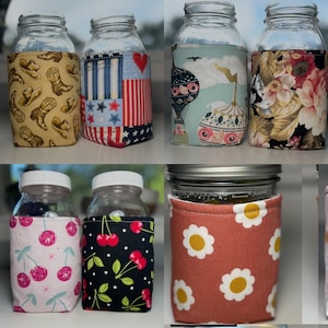 K&ouml;nnte beinhalten: Eine Sammlung von Einmachgl&auml;sern aus Glas mit verschiedenen Stoffh&uuml;llen, die Muster wie Cowboystiefel, patriotische Sterne und Streifen, Hei&szlig;luftballons, Blumen, Disco-Kirschen und wei&szlig;e G&auml;nsebl&uuml;mchen auf terrakottafarbenem Grund zeigen.