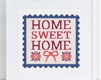 Op de afbeelding: Een ingelijst kruissteekkunstwerk met de woorden "HOME SWEET HOME" in rode letters. Het ontwerp bevat roze bloemen en een rode strik op een lichtroze achtergrond, omlijst door een blauwe rand en een witte lijst.