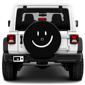 May include: A white Jeep Wrangler with a black spare tire cover featuring a white smiley face.