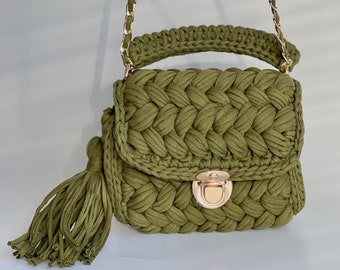 May include: An olive green crochet handbag with a gold chain strap and clasp. The bag has a braided design on the front flap and a matching tassel. The handle is also crocheted. A stylish accessory.