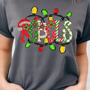 May include: A dark gray t-shirt with the word "RUGLS" in a festive design. The letters are decorated with Christmas lights, red and green patterns, and a Santa hat. The shirt is a comfortable, casual style.