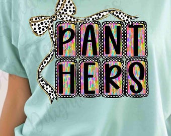 Può includere: T-shirt azzurra con la scritta "PANTHERS" in un design a blocchi colorati. Le lettere sono bordate in bianco e nero, con un fiocco a pois in alto.