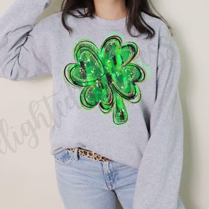 May include: A gray sweatshirt with a green, gold, and black shamrock design. The shamrock is a four-leaf clover with a plaid pattern.