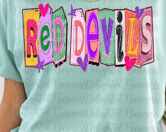 Op de afbeelding: Een lichtblauw t-shirt met de tekst "RED DEVILS" in een kleurrijk 3D-blokletterontwerp. De letters zijn zwart omlijnd en versierd met hartjes en sterren.