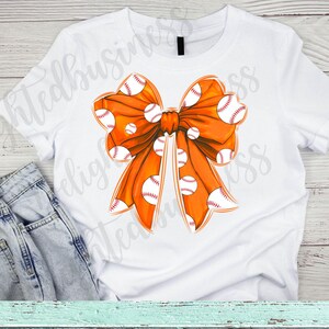 May include: Orange bow with white baseballs printed on it. The bow is on a white t-shirt.