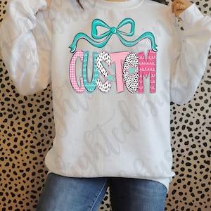 May include: White sweatshirt with a blue bow and the word "CUSTOM" in pink, black and white patterned letters.