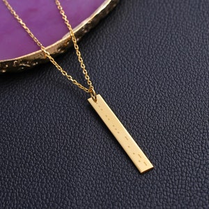 May include: A gold necklace with a long, thin bar pendant engraved with a message in braille.