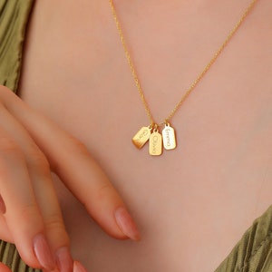 May include: Gold necklace with three small rectangular tags, each engraved with a name: Emma, Olivia, and Chloe.