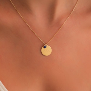 May include: Gold necklace featuring a round pendant engraved with the name "Ella" and a small blue gemstone.