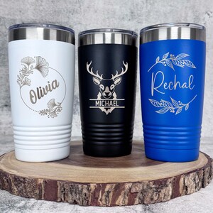 May include: Three stainless steel tumblers with personalized engravings. The white tumbler has a floral design and the name "Olivia". The black tumbler has a deer silhouette and the name "Michael". The blue tumbler has a floral design and the name "Rachel".