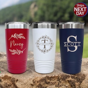 May include: Three stainless steel tumblers with personalized engravings. The tumblers are red, white, and blue. The red tumbler has a floral design and the name "Nancy" engraved on it. The white tumbler has a floral wreath design and the name "Tiffany" engraved on it. The blue tumbler has a split monogram design with the letter "S" and the name "Scott" engraved on it.
