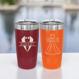 May include: Two personalized stainless steel tumblers. The tumbler on the left is burgundy with a tuxedo graphic and the name "ROBERT". The tumbler on the right is orange with a dress graphic and the name "MEGAN".