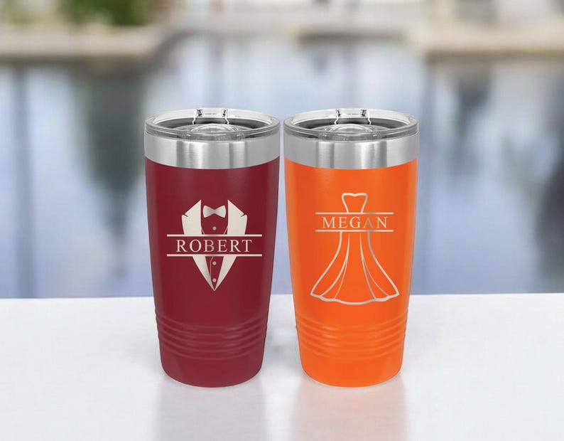 May include: Two personalized stainless steel tumblers. The tumbler on the left is burgundy with a tuxedo graphic and the name "ROBERT". The tumbler on the right is orange with a dress graphic and the name "MEGAN".