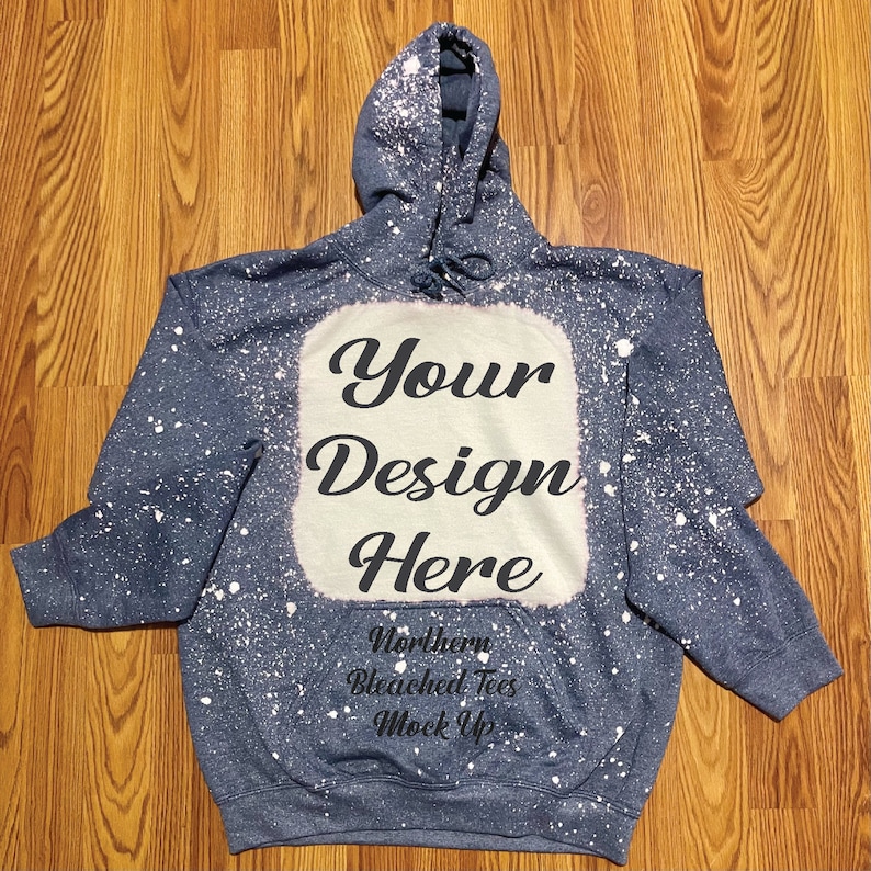 Puede incluir: Una sudadera con capucha azul con un dise&ntilde;o blanqueado y el texto "Your Design Here". La sudadera tiene una capucha con cord&oacute;n y un bolsillo delantero. Tambi&eacute;n se ve el texto "Northern Bleached Tees Mock Up".