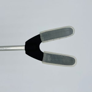 May include: A black and silver tool with two clear plastic tips. The tool is attached to a silver metal rod.