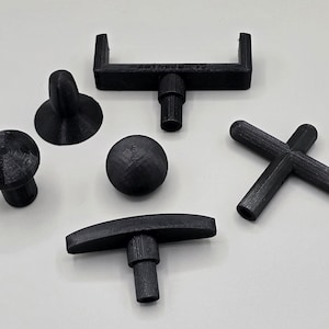 Peut inclure: Un ensemble de six boutons en plastique noir de formes différentes, dont un bouton rond, un bouton en forme de croix, un bouton en forme de T, un bouton avec un dessus en forme de U et deux boutons avec un dessus rond et une base.