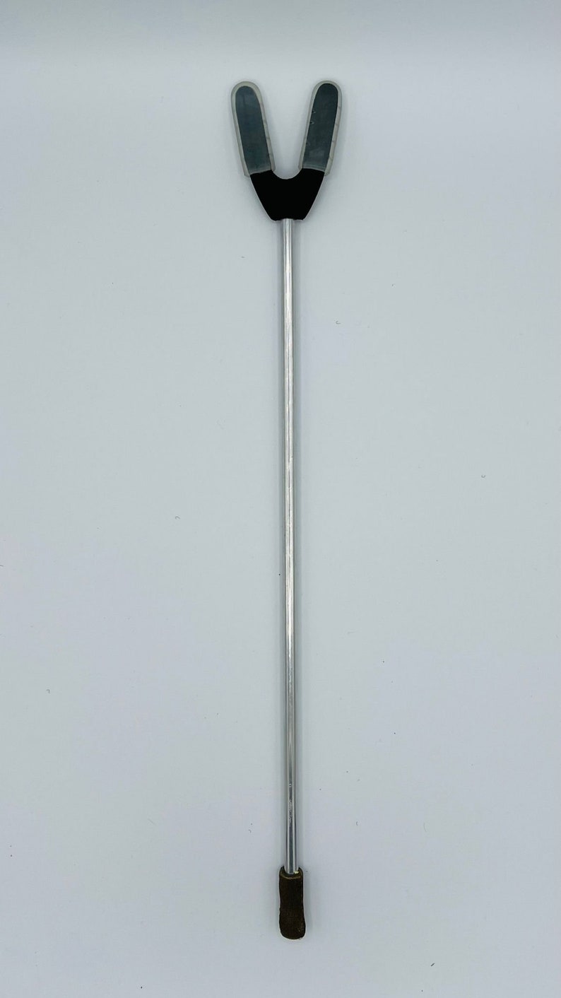 May include: A silver metal tongue depressor with a black rubber tip and two gray rubber flaps at the top.