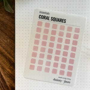 May include: A sheet of coral-colored square stickers with the text "essentials CORAL SQUARES" and "made in the US by dainty + favors".