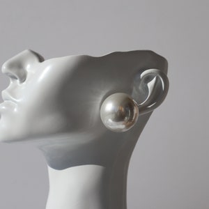 Könnte beinhalten: Ein Paar silberne Creolen mit einer großen, runden, perlmuttartigen Kugel, die an jedem Creolen befestigt ist.