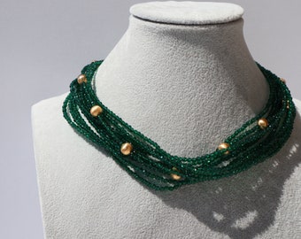 May include: A multi-strand necklace made of dark green beads with gold accents. The necklace is displayed on a white mannequin.