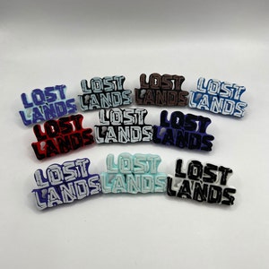May include: Nine different color variations of a small, plastic pin with the words "Lost Lands" in black lettering.