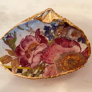 May include: A decorative shell dish with a gold rim and a floral pattern. The shell is painted with a white background and features pink, red, and yellow flowers.