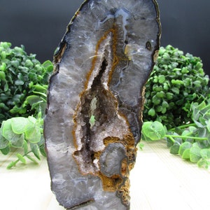 May include: A large, grey and brown agate geode with a hollow centre and white crystals. The geode is polished and has a smooth surface.
