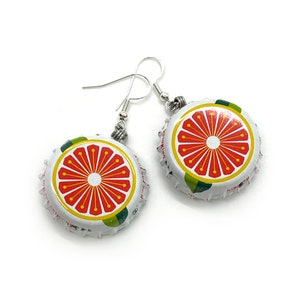 May include: A pair of earrings made from repurposed bottle caps. The bottle caps are white with a green and yellow border and a red grapefruit design. The earrings are attached to silver hooks.