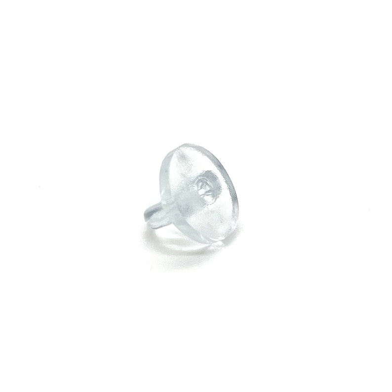 May include: A clear, transparent earring back, also known as a clutch, is shown against a white background. The earring back has a disc shape with a small post extending from one side. The post is designed to fit into the earring post.